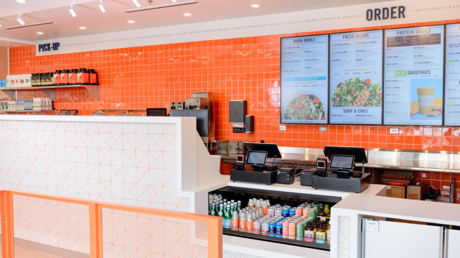 Interior of a Protein Bar & Kitchen restaurant showing the order counter, menu boards and orange tile